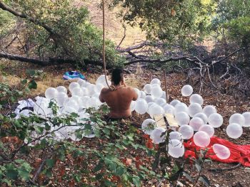 Still from performance in Elysian Park STILL, 2012, soil, artist's breath, translucent white balloons, jute rope noose, shovel, cardboard box. Rafael Esparza